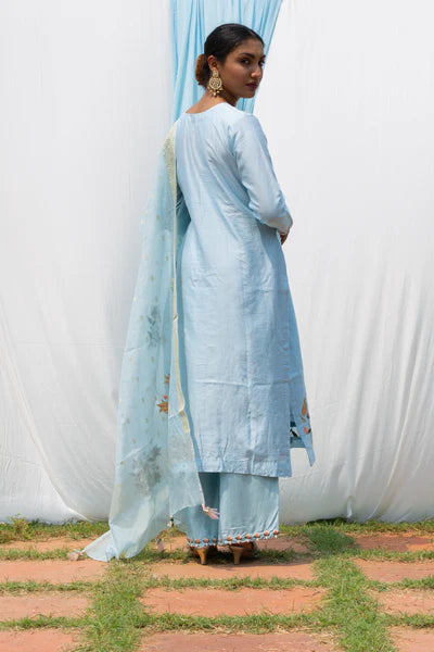 A woman standing and wearing Rajkumari Light Blue Colored Suit Set.