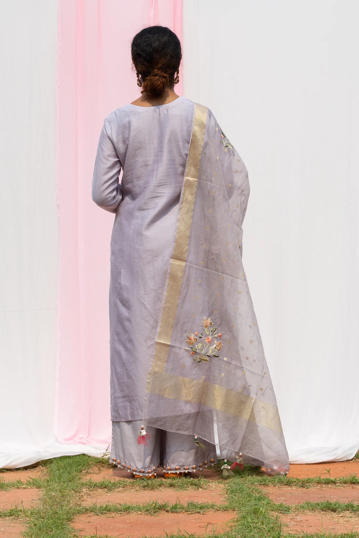 A woman standing and wearing Rajkumari Light Grey Colored Suit Set.