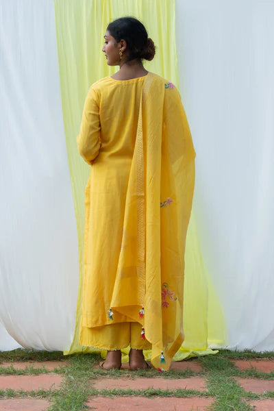 A woman standing and wearing Titli Yellow Colored Suit Set.