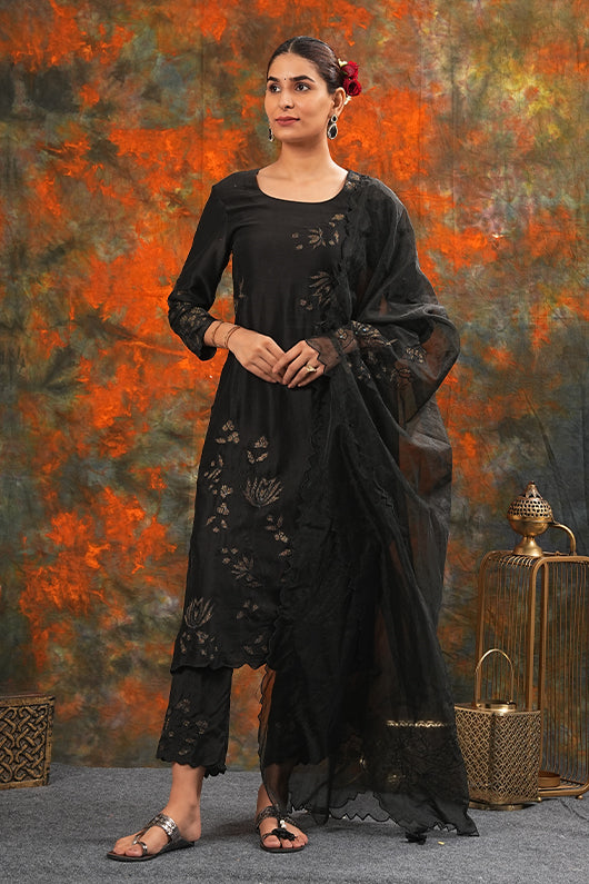 A woman standing and wearing black colored suit with pants and dupatta.