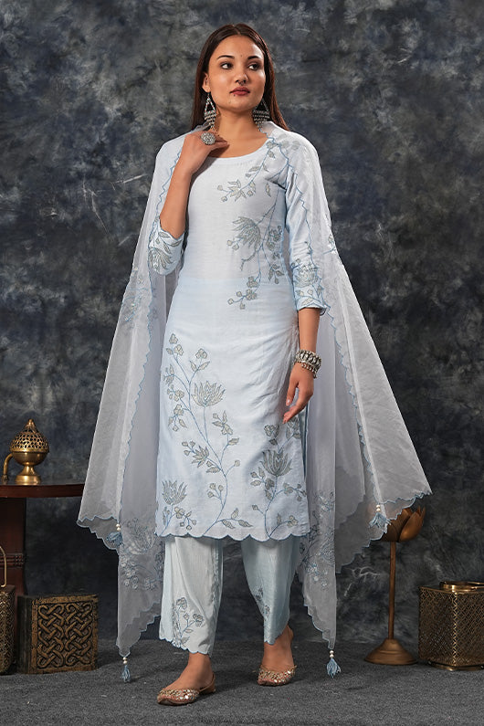 A woman standing and wearing sky blue colored suit with pants and dupatta.