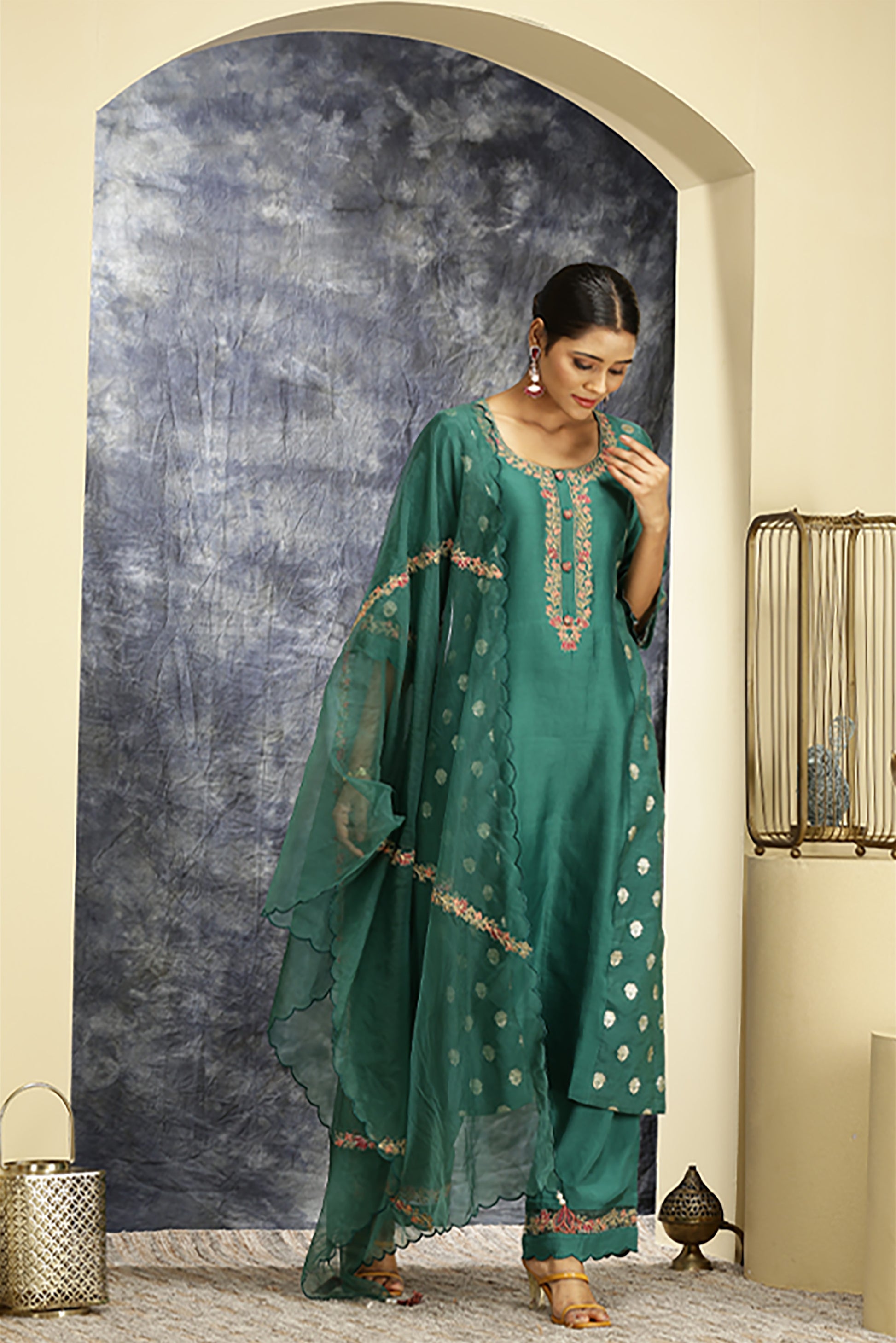 A woman standing and wearing green colored suit with pants and dupatta.