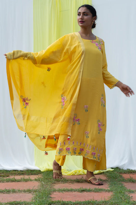 A woman standing and wearing Titli Yellow Colored Suit Set.